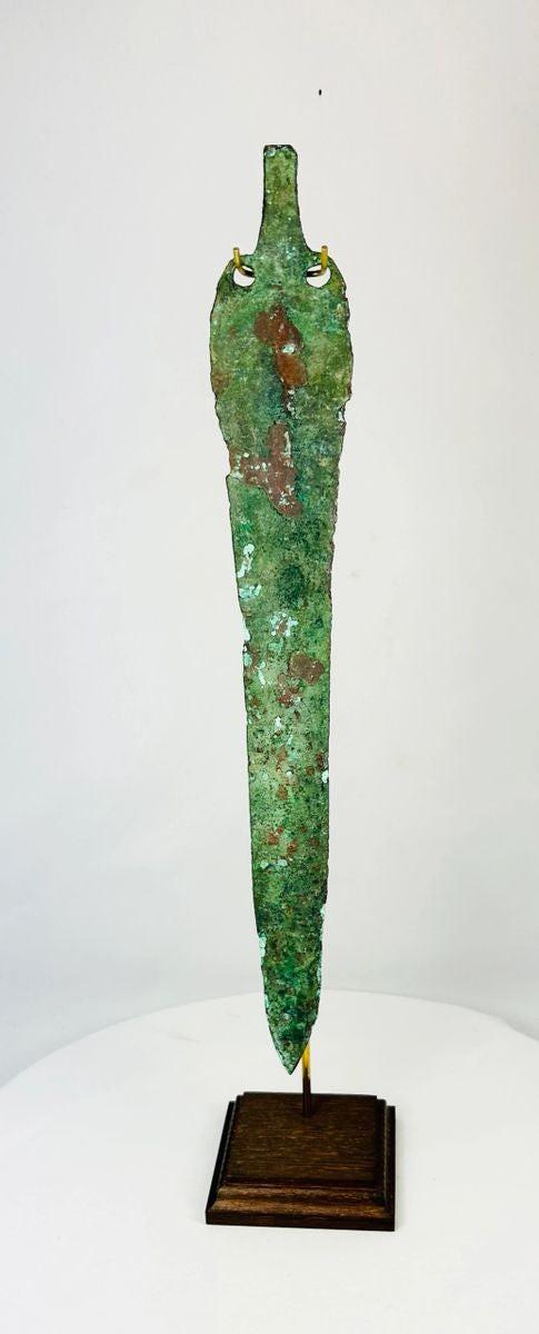Ancient Bronze Age blade from the Caspian region, circa 2000–1000 BCE, with tapered elongated form, two perforations near the hilt, and rich green patina, mounted on a custom stand.