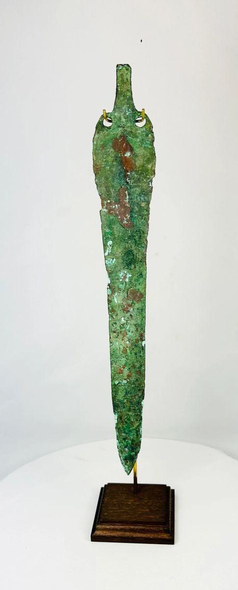 Ancient Bronze Age blade from the Caspian region, circa 2000–1000 BCE, with tapered elongated form, two perforations near the hilt, and rich green patina, mounted on a custom stand.