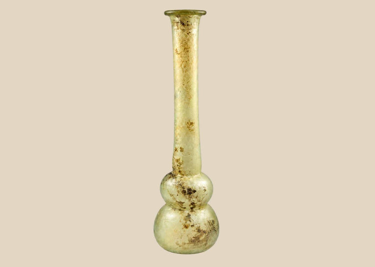 Ancient Roman clear glass double gourd balsamarium from the Eastern Mediterranean, 2nd–3rd Century CE. Features two globular sections joined by a slender neck, naturally iridescent patina, and substantial size for holding perfumes or balms. Reflects Roman glassmaking sophistication, luxury, and daily bathhouse culture.
