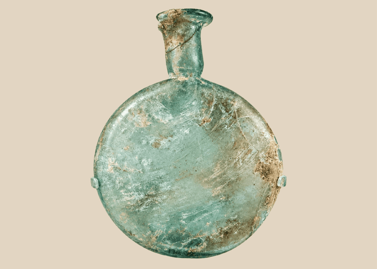 Ancient Roman pale green glass flask with flattened body and long neck displayed on acrylic stand