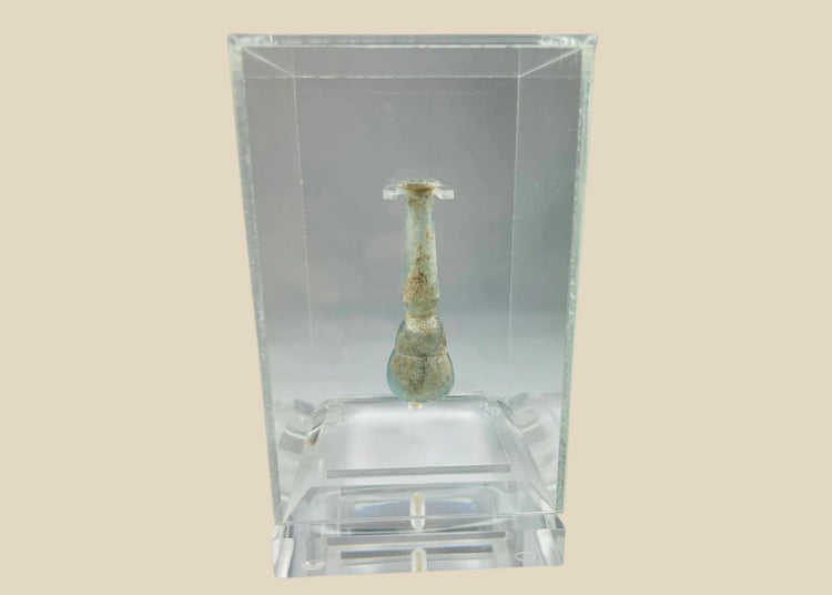 Ancient Roman pale turquoise blown glass balsamarium, 2nd–3rd Century CE. Double-gourd body with tapering neck and outfolded lip, featuring natural iridescent patina. Hand-blown vessel used for perfumes, ointments, and luxury grooming, reflecting Roman craftsmanship, refinement, and elite culture.