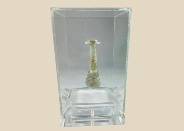 Ancient Roman pale turquoise blown glass balsamarium, 2nd–3rd Century CE. Double-gourd body with tapering neck and outfolded lip, featuring natural iridescent patina. Hand-blown vessel used for perfumes, ointments, and luxury grooming, reflecting Roman craftsmanship, refinement, and elite culture.