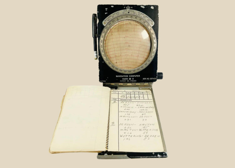 RAF WWII navigational computer with rotating aluminum dial, Bakelite adjustments, original fabric straps, pencil, and open flight notebook showing handwritten navigator’s notes.