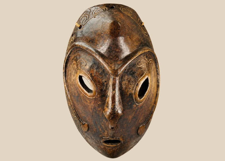 Early 20th-century Sepik River tribal ceremonial mask, hand-carved from wood with elongated oval form, large almond-shaped eyes, incised swirling patterns, and traces of natural pigments, mounted on a display stand; traditional artifact used in ancestral rituals and cultural ceremonies of Papua New Guinea.