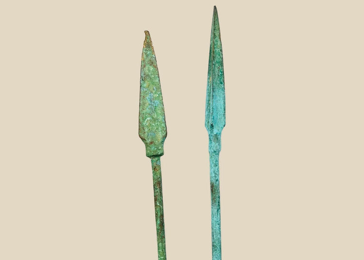 Ancient bronze spearheads with leaf-shaped tapered forms and rich green patina, mounted on black display stands, dating to the Bronze or Iron Age (2nd–1st millennium BCE).