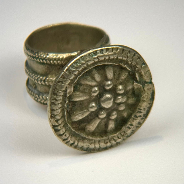Antique silver-toned ring with circular floral bezel, detailed relief work, and natural surface patina