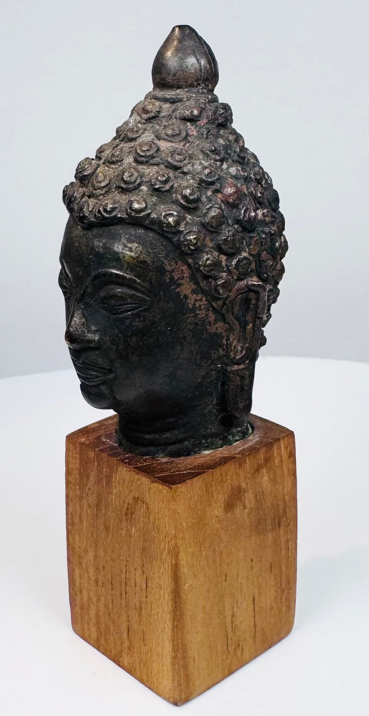 Antique bronze Buddha head with serene expression, closed eyes, and detailed hair curls