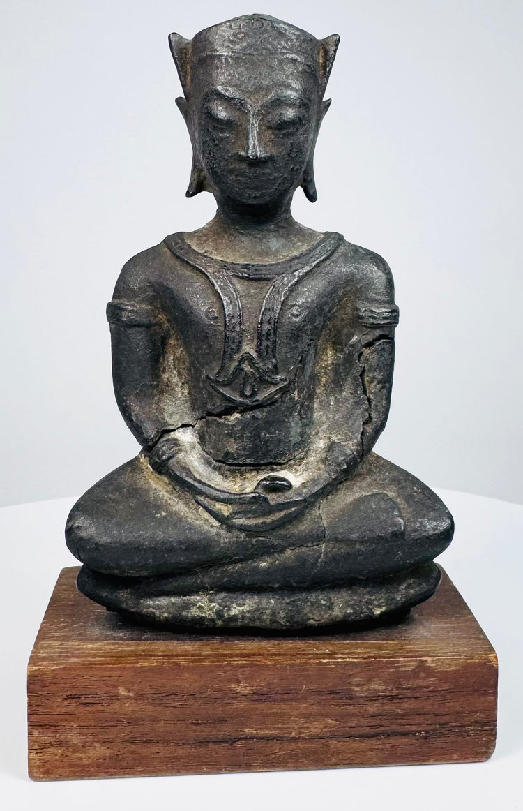 Seated bronze Buddha displaying raised chest decoration, rounded shoulders, and folded hands above crossed legs.