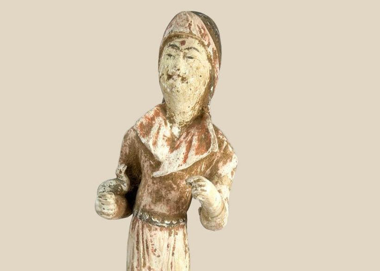 Tang Dynasty low-fired terracotta figure of a female court attendant, standing with hands clasped, wearing flowing robes with traces of red and white pigments, serene expression, Tang hairstyle, 13 inches tall, surface mineral deposits and patina, circa 618–907 CE.
