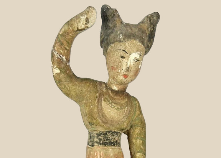 Tang Dynasty low-fired terracotta figurine of a female dancer, mid-performance pose with raised arm, twin-knot chignon hairstyle, traces of original red-orange and black mineral pigments on robe and facial features, mounted on a wooden display base, 11 inches tall, circa 618–907 CE.