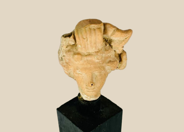 Ancient terracotta head fragment from the Greco-Roman world, circa 4th–1st Century BCE, showing naturalistic facial features and elaborate hairstyle, mounted on a modern black display base, Hellenistic and classical artistic style.