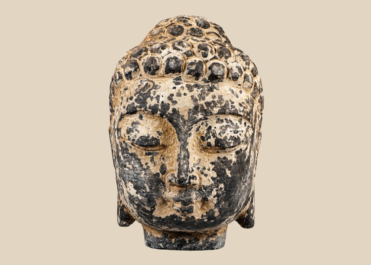 Carved stone Buddha head sculpture with serene expression and curled hair on marble base