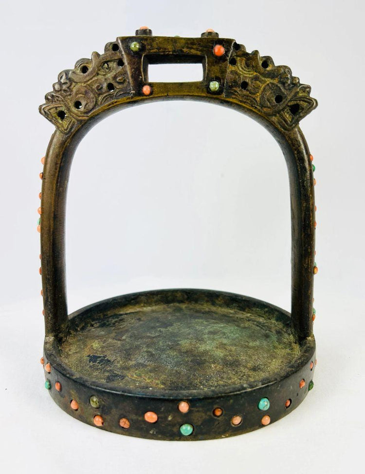 Antique Mongol–Tibetan bronze saddle stirrup with coral and turquoise inlay, upright view on white background.