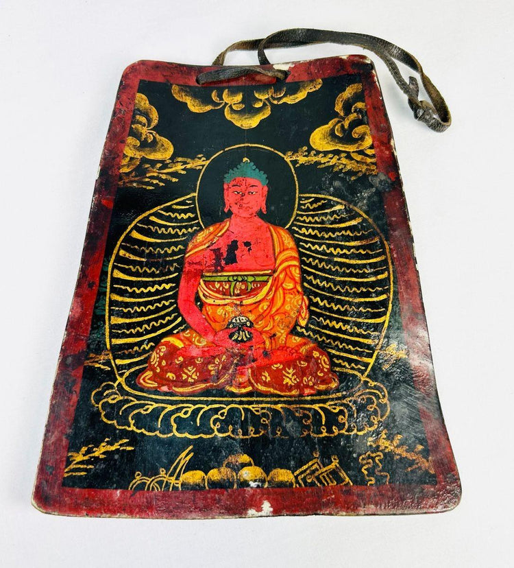 Late Qing Dynasty Tibetan devotional plaque, circa 19th century, hand-painted with vivid polychrome depiction of a seated Buddha in red and gold robes, surrounded by radiant aureole and cloud motifs; crafted on a rectangular wooden panel with suspension cord, showing surface wear and patina from ritual use.