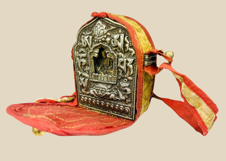 18th–19th century Tibetan Gau shrine, silvered copper alloy with repoussé seated Buddha, gilt backing plate, and original red fabric strap, portable Himalayan Buddhist amulet box