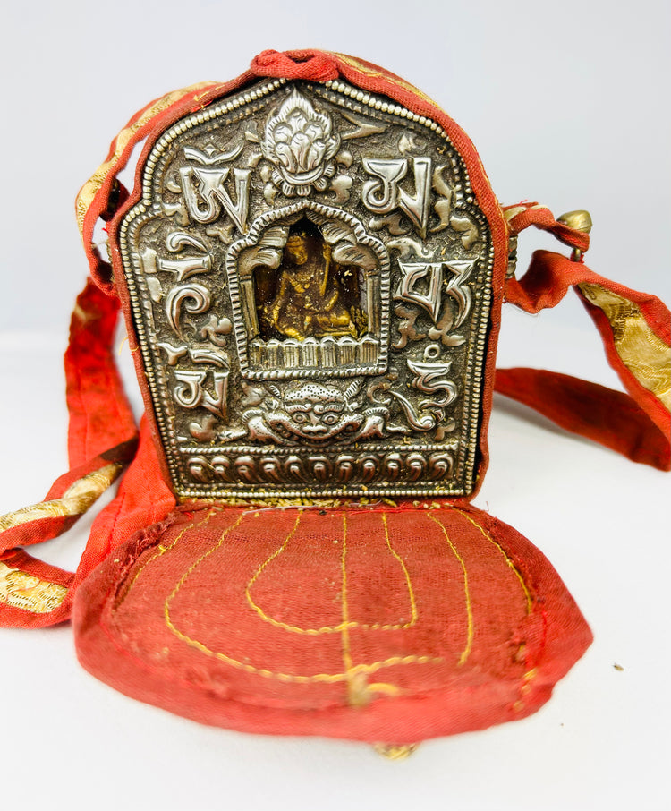 18th–19th century Tibetan Gau shrine, silvered copper alloy with repoussé seated Buddha, gilt backing plate, and original red fabric strap, portable Himalayan Buddhist amulet box