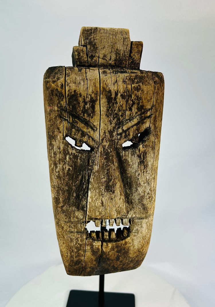 Close-up of facial details on hardwood mask revealing carved teeth, brow ridges, and surface fissures.