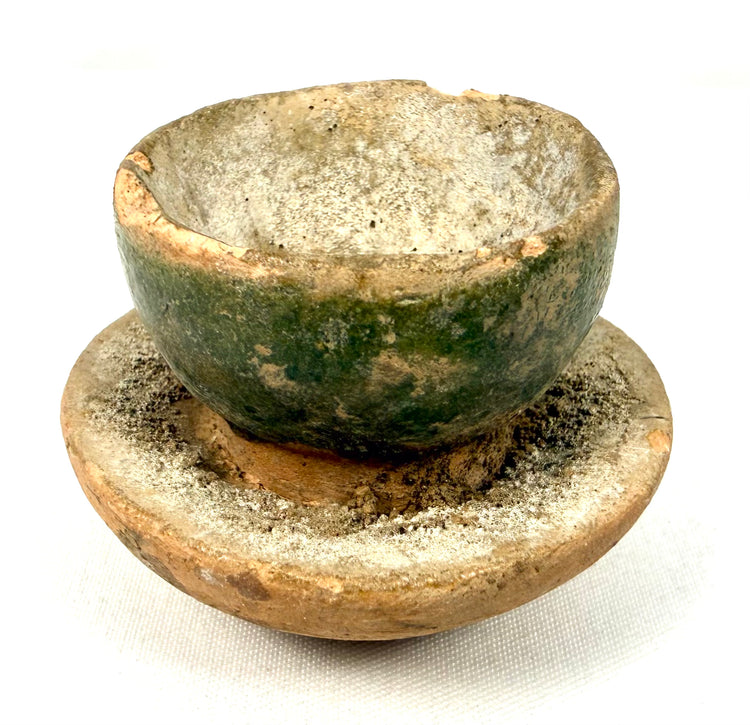 Miniature East Asian green-glazed ceramic cup with pedestal stand, aged surface, rim chipping, and traces of original glaze.