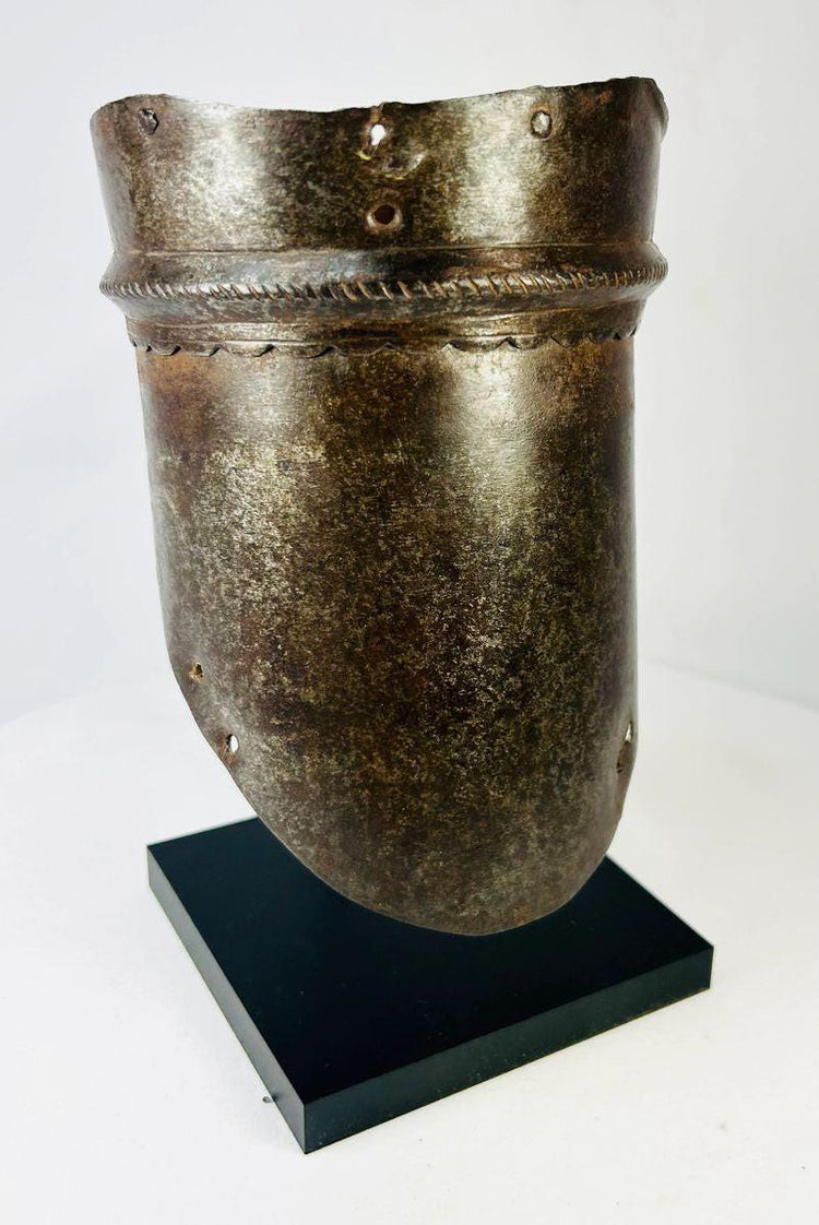 16th-century European upper arm armor, cannon-style plate with scalloped edge detailing, aged patina, and mounted on a display stand.