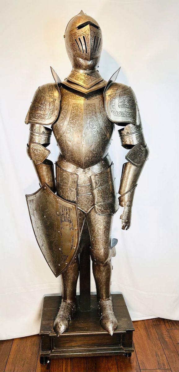 Victorian-era full suit of armor, early 19th century, 80 inches tall by 32 inches wide. Acid-etched metal plates decorated with intricate engravings of mythical creatures, dragons, crowns, battle scenes, and scrolling foliage. Inspired by 15th-century medieval armor, reflecting Victorian fascination with chivalric ideals and Gothic artistry. Mounted on a custom wooden display stand.