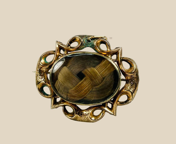 Antique Victorian mourning brooch with braided human hair under beveled glass, set in an ornate gold-plated brass Gothic Revival frame, circa 1850–1880.