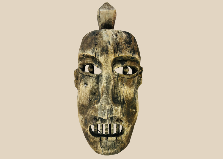 Front view of an aged wooden ritual mask displayed on a museum-style stand against a white background.