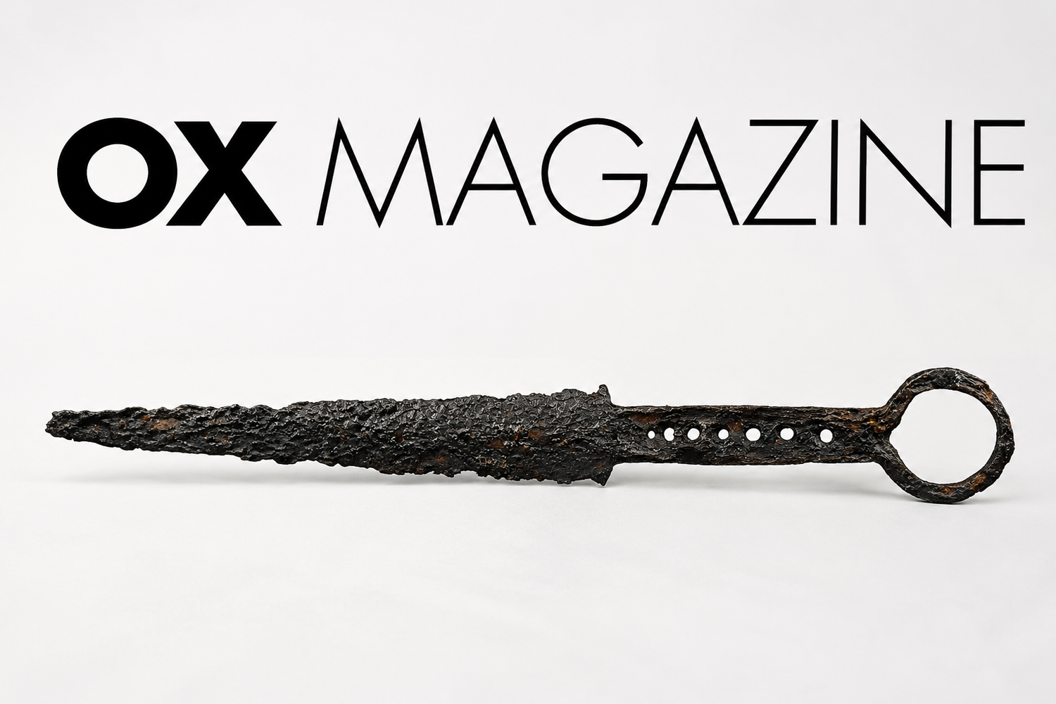 Ancient corroded iron dagger displayed beneath the OX Magazine logo on a minimalist editorial-style background, representing historical dagger collecting, rarity, and antique weapon authenticity.
