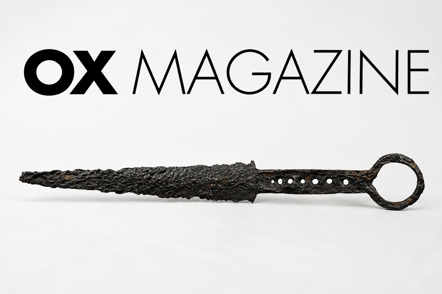 Ancient corroded iron dagger displayed beneath the OX Magazine logo on a minimalist editorial-style background, representing historical dagger collecting, rarity, and antique weapon authenticity.