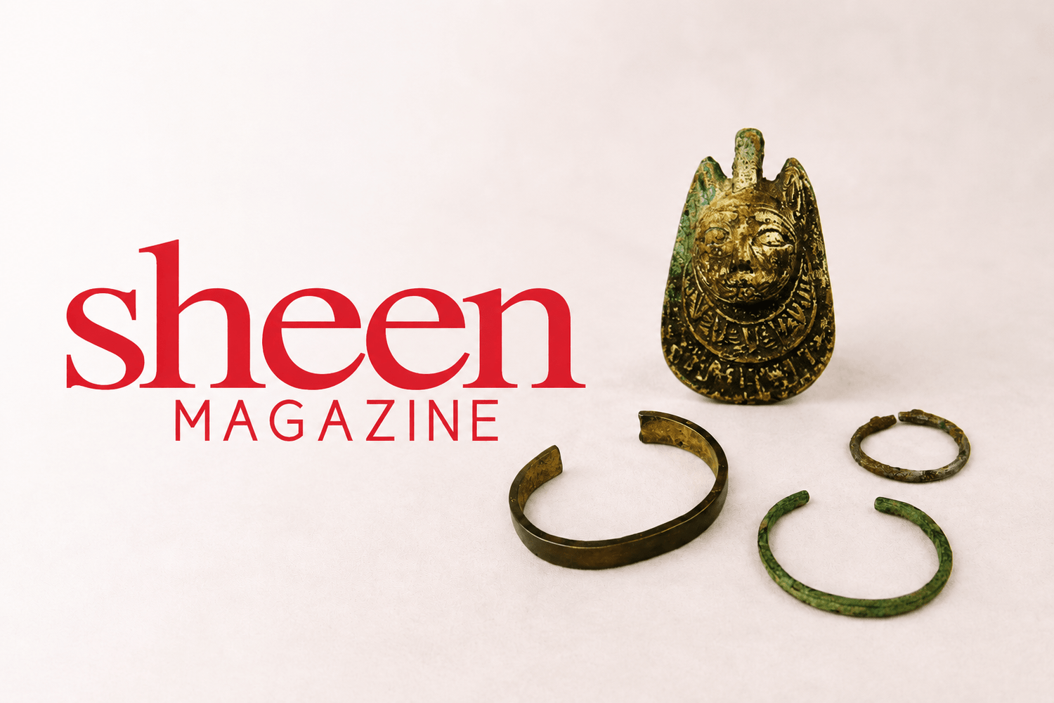 Ancient bronze and copper artifacts arranged on a soft neutral studio background beside the red Sheen Magazine logo, featuring a weathered patinated amulet and three ancient bracelets with visible age and oxidation.