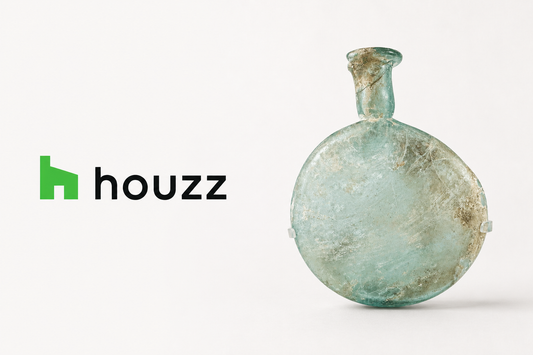 Houzz logo beside an ancient Roman pale green glass flask, featured by Relic & Rarity for an article on integrating Greco-Roman antiquities into luxury interiors.