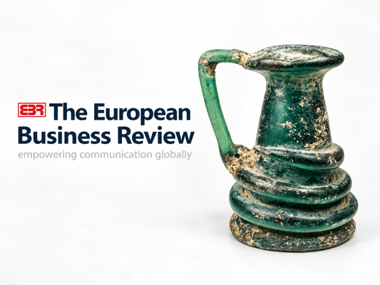 Relic & Rarity featured in The European Business Review, alongside an ancient Roman green glass vessel with a curved handle, applied spiral decoration, and naturally aged patina.
