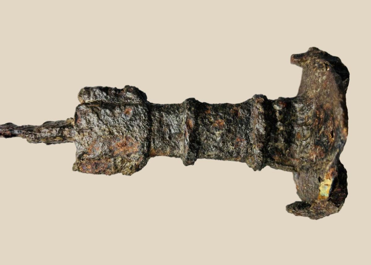 Ancient Iron Age sword fragment with heavy corrosion and preserved hilt section.