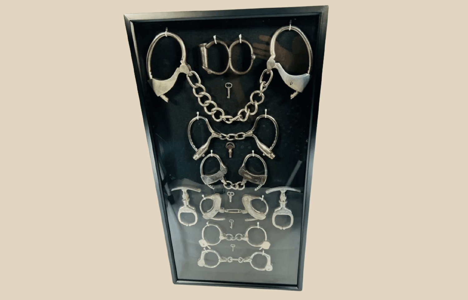 Framed collection of antique handcuffs and historical restraint devices from the 19th–20th century.