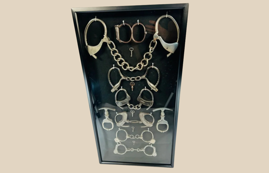 Framed collection of antique handcuffs and historical restraint devices from the 19th–20th century.