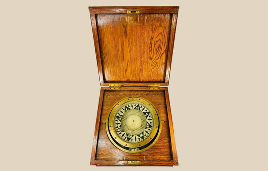 Antique ship’s compass in a wooden box, early 20th-century maritime navigation instrument.