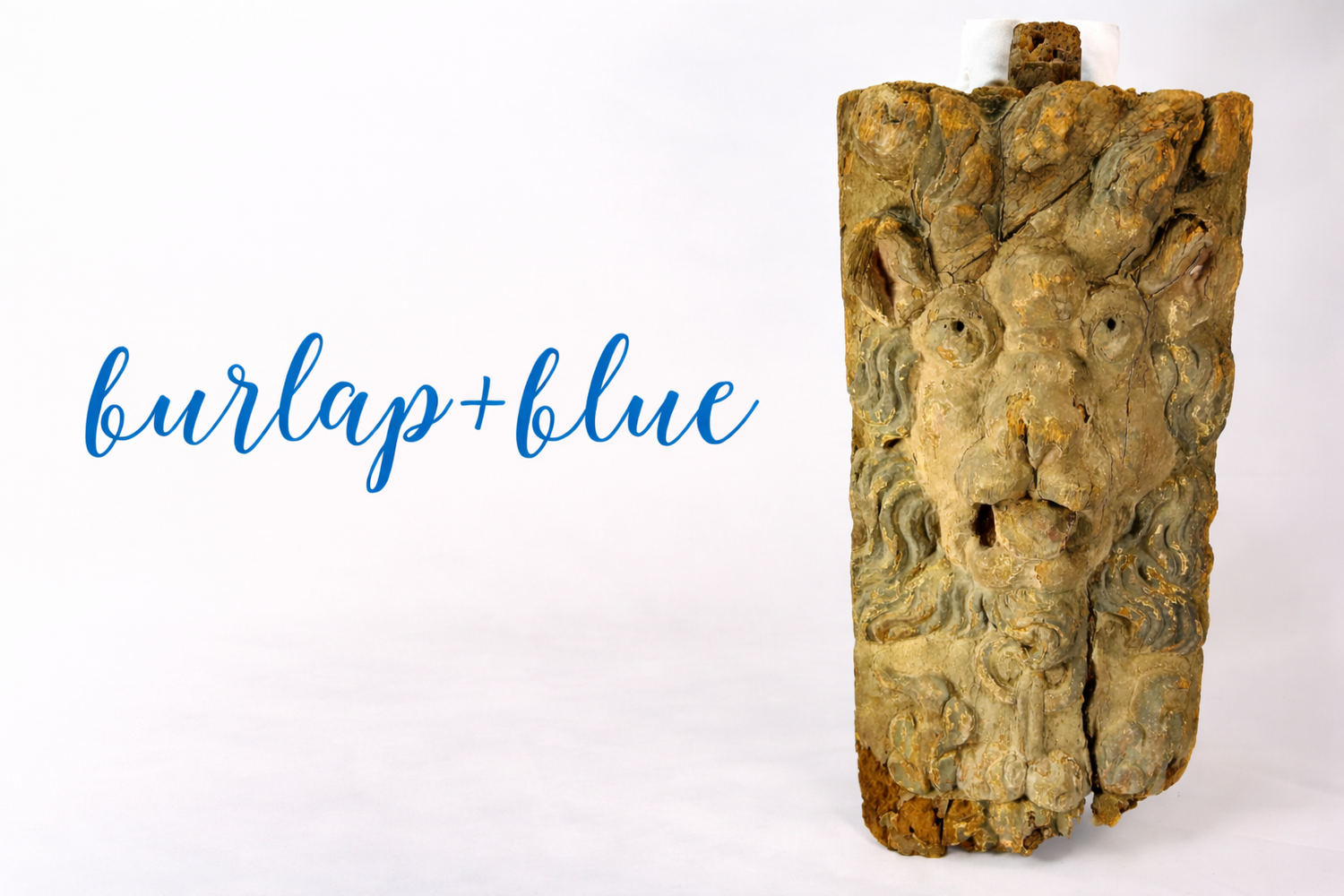 Burlap + Blue publication logo displayed beside a carved antique wooden lion architectural fragment with aged paint and weathered surface against a neutral studio background.