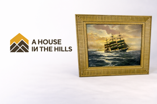 Logo of A House in the Hills beside a framed antique maritime oil painting of a sailing ship at sea.