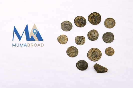 MUMABROAD travel publication logo displayed beside a collection of ancient Roman bronze coins arranged on a clean white studio background.