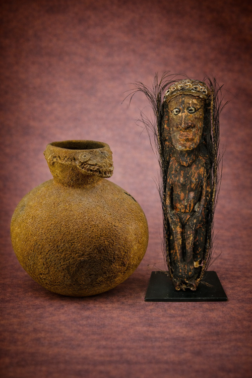West African terracotta crocodile-head vessel beside Papua New Guinea ancestor spirit figure on studio backdrop.