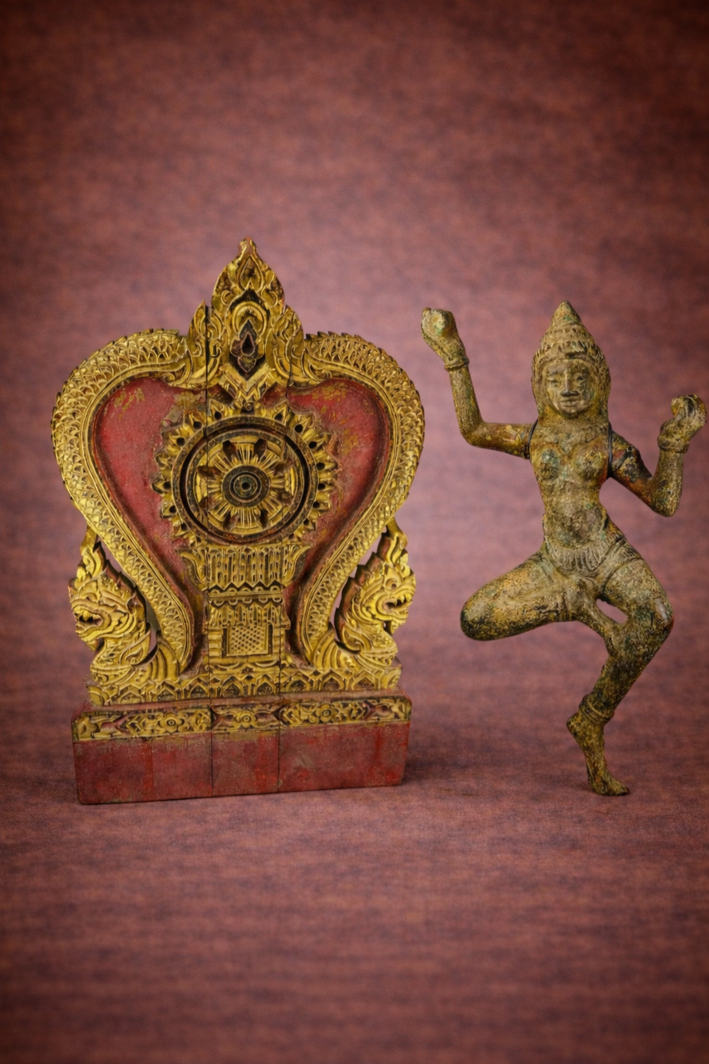 Gilded Thai temple panel with Dharmachakra beside a bronze South Asian dancing deity statue on a warm studio background.