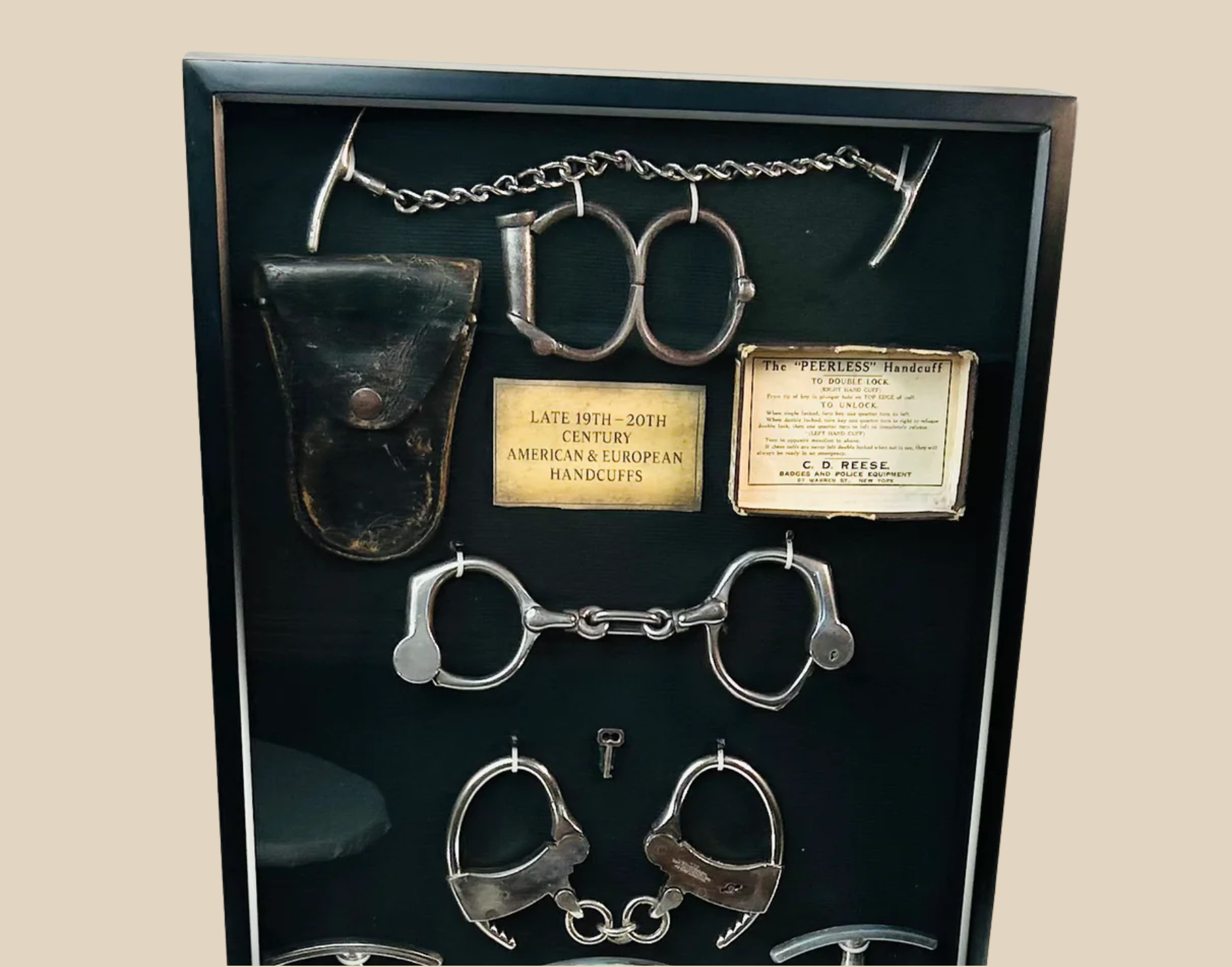 Framed display of antique shackles, handcuffs, and leg irons with original identification tags and leather pouch