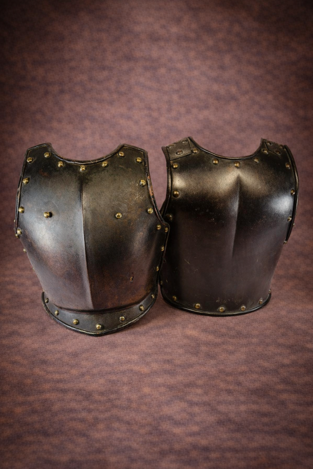 Front and back plates of a 19th-century French cuirassier armor set displayed side by side against a warm brown studio background.