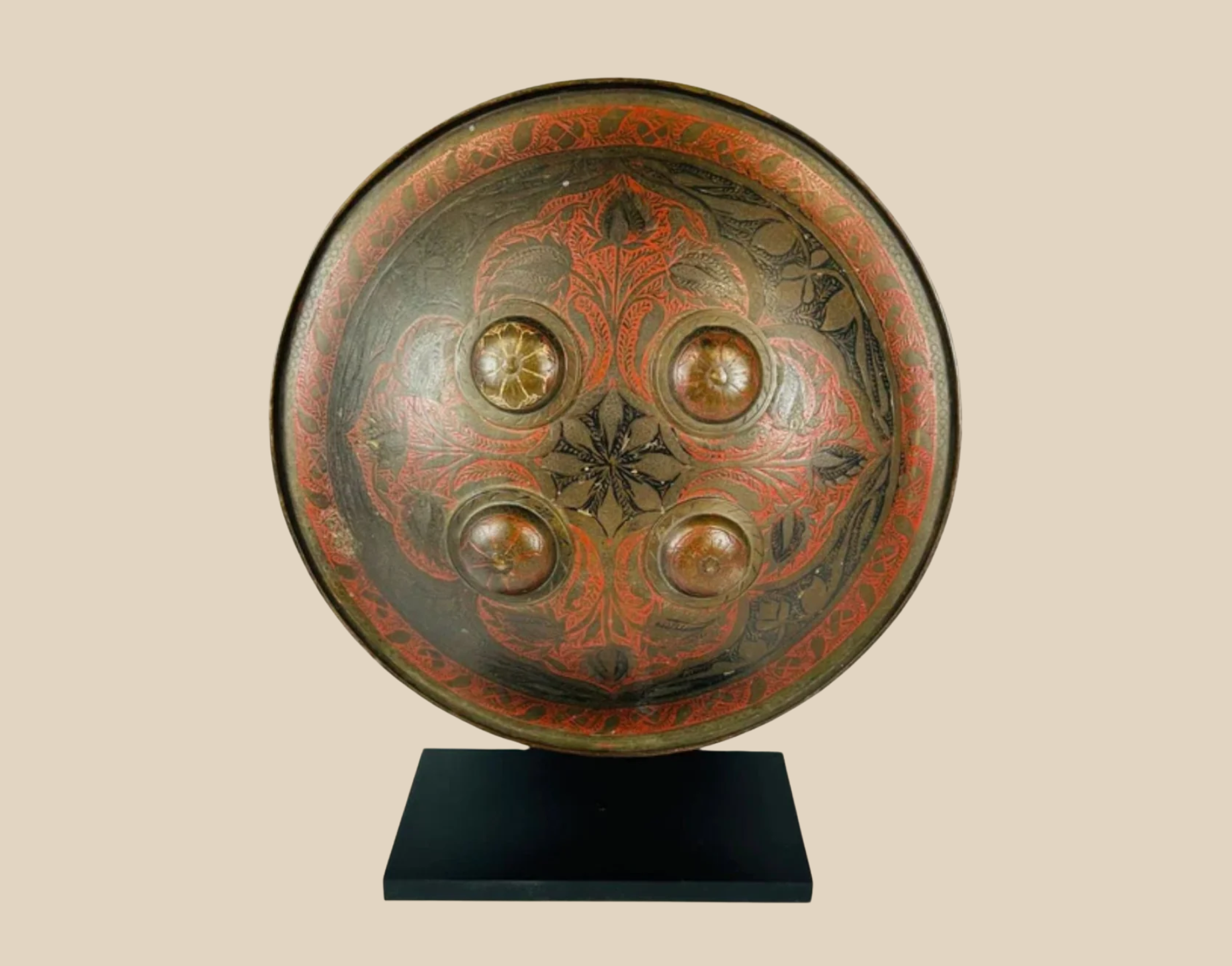 Antique painted wooden shield with central brass bosses and red-and-black geometric motifs on display stand