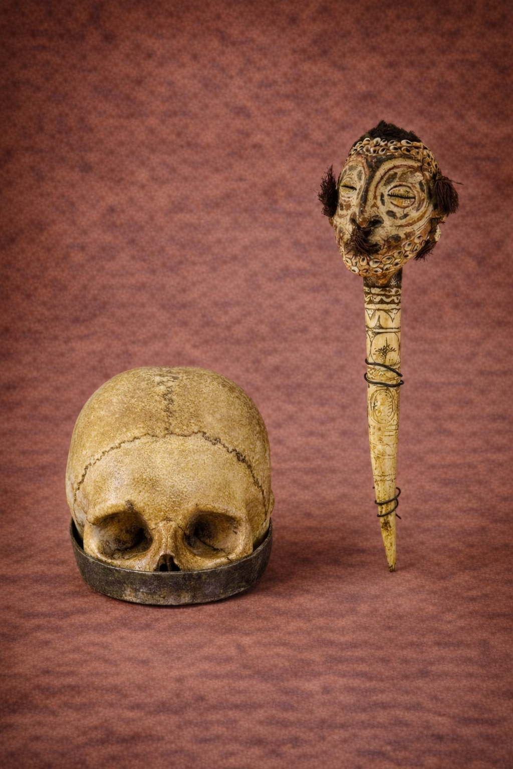 Tibetan Buddhist kapala ritual skull cup with natural cranial sutures and aged patina, resting in a metal base against a warm textured studio backdrop.