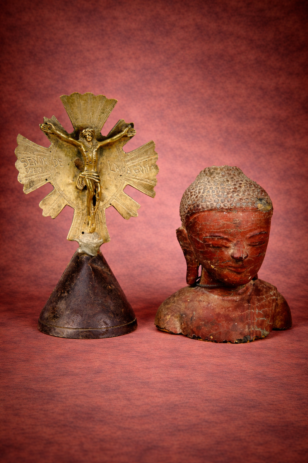 Spanish Colonial brass crucifix and Southeast Asian Buddha bust displayed against a warm studio background.