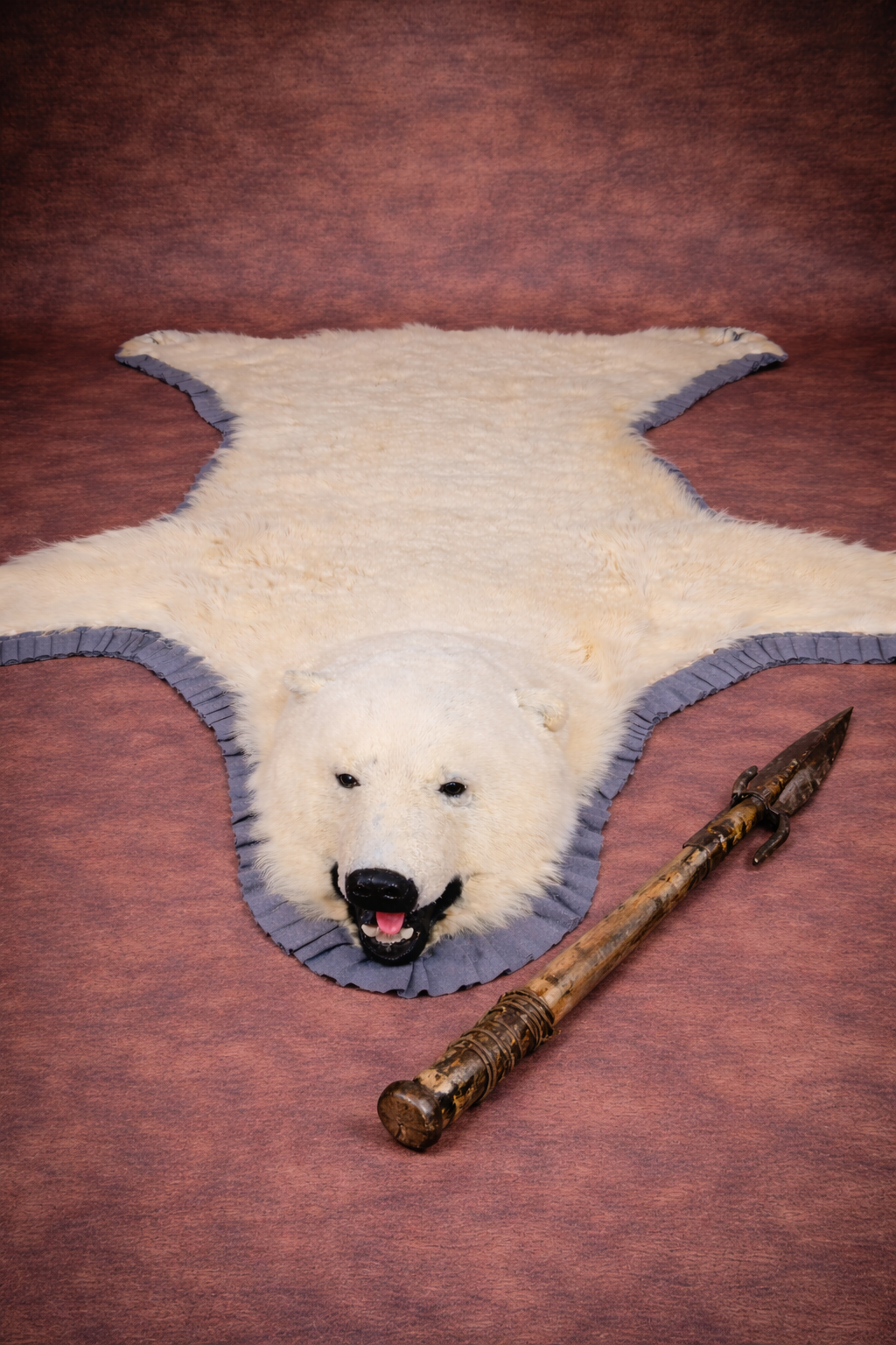 Polar bear rug displayed on a warm brown studio background with an antique harpoon placed beside it.