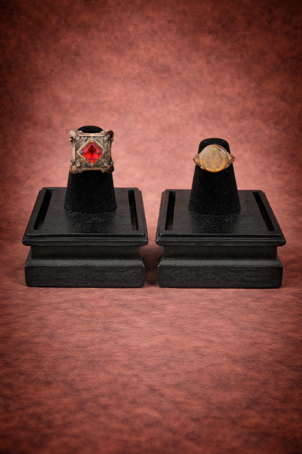 Antique silver tribal ring with colored enamel bezel and Indo-Greek carved gemstone ring displayed on black presentation stands against a neutral background.