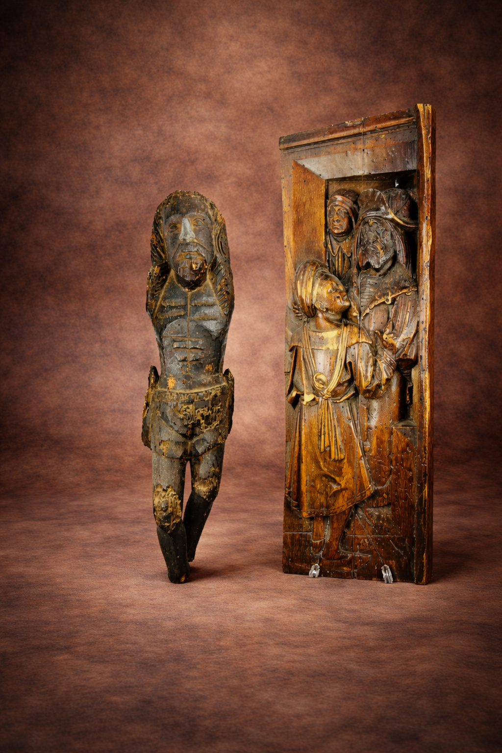 16th-century Spanish Colonial carved wooden Christ figure displayed beside an early English Tudor Gothic carved oak panel relief against a studio backdrop.