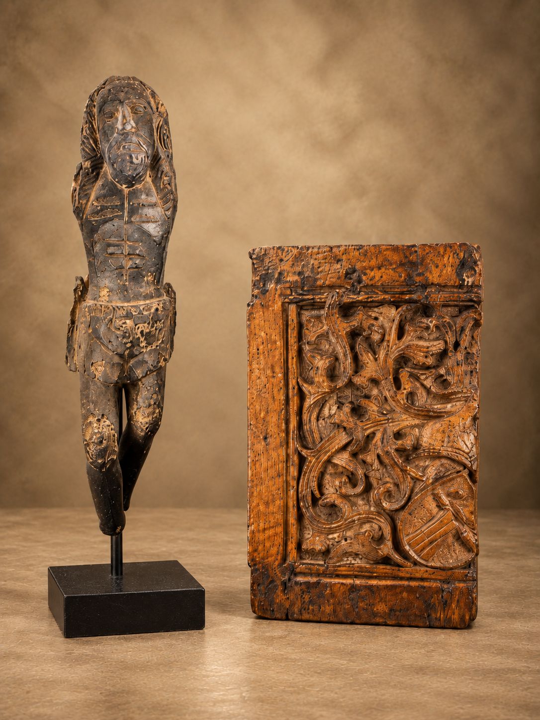 16th-century artifacts featuring a carved standing figure beside an ornate wooden panel with heraldic and scrolling decorative motifs.