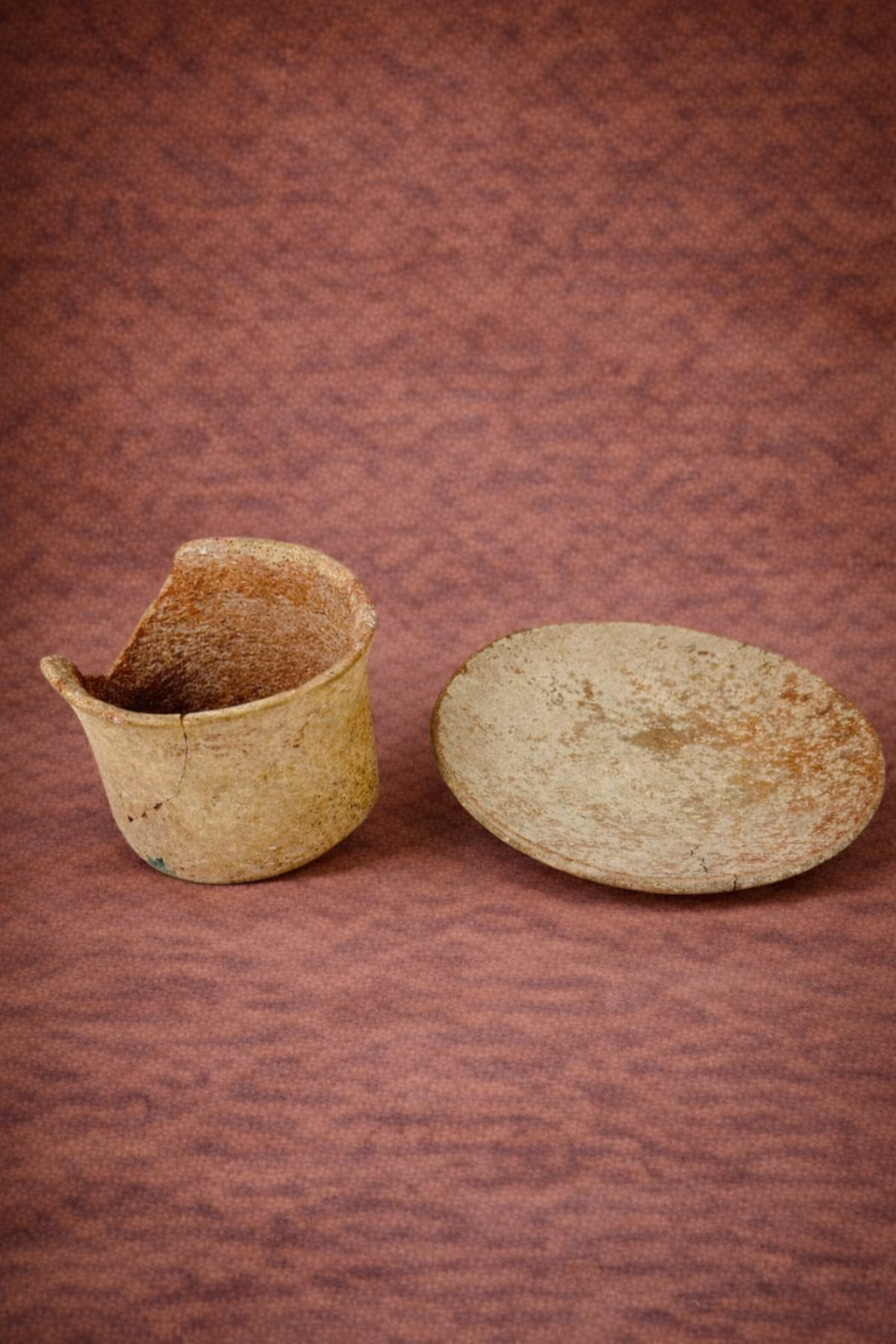 Neolithic pottery vessel fragment and shallow ceramic bowl displayed side by side against a warm textured studio backdrop, showing age wear and surface patina.